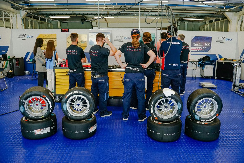 Motorsport garage scene with mechanics preparing for a race, featuring multiple tire compounds and tools.
