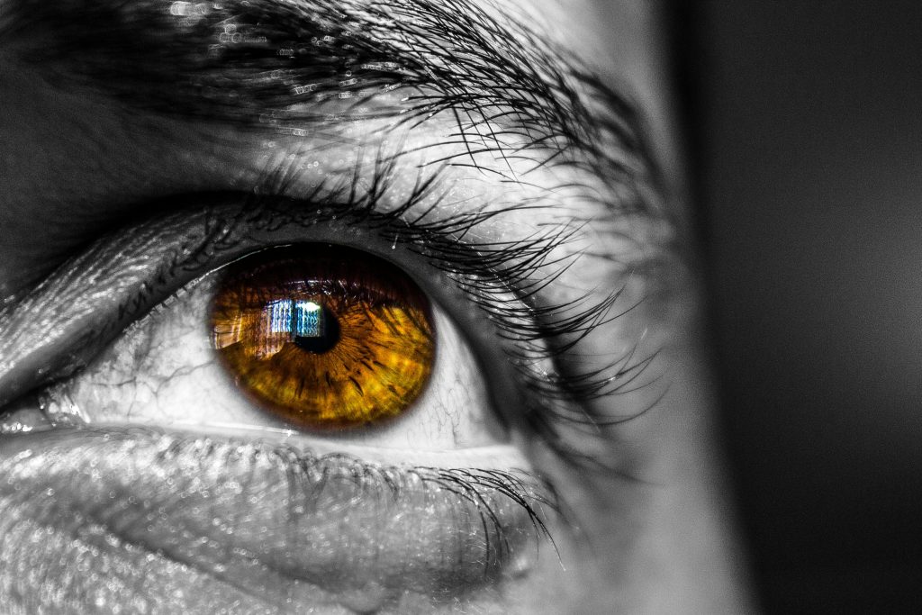 Detailed close-up image of a human eye, showcasing an amber-colored iris with architectural reflection.